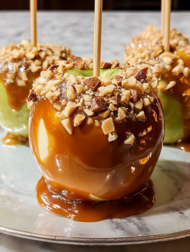 Three caramel apples with sticks in them.