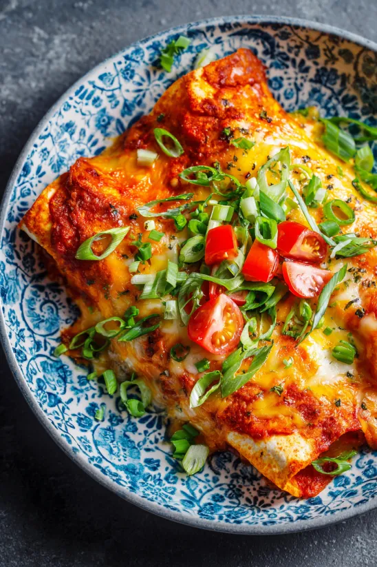 A plate of cheese enchiladas with green onions on top.