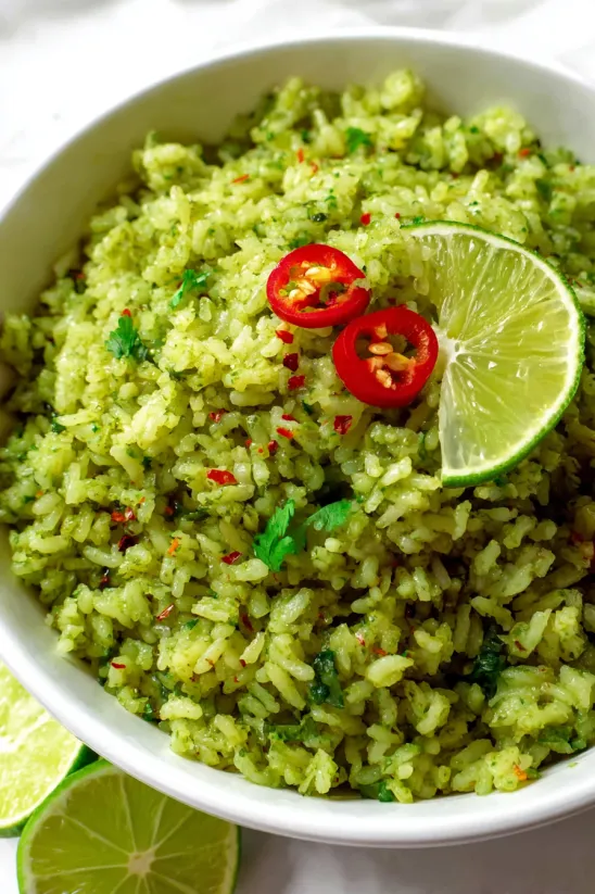 A bowl of green rice with red peppers on top.
