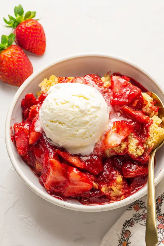 A bowl of strawberry dump cake with a scoop of ice cream on top.