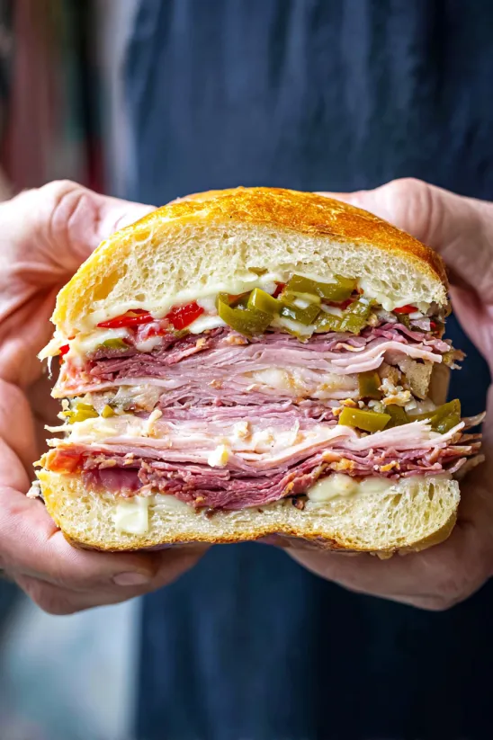 A person holding a muffaletta sandwich.