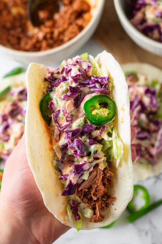 A hand holding a corned beef taco with a creamy cabbage slaw.