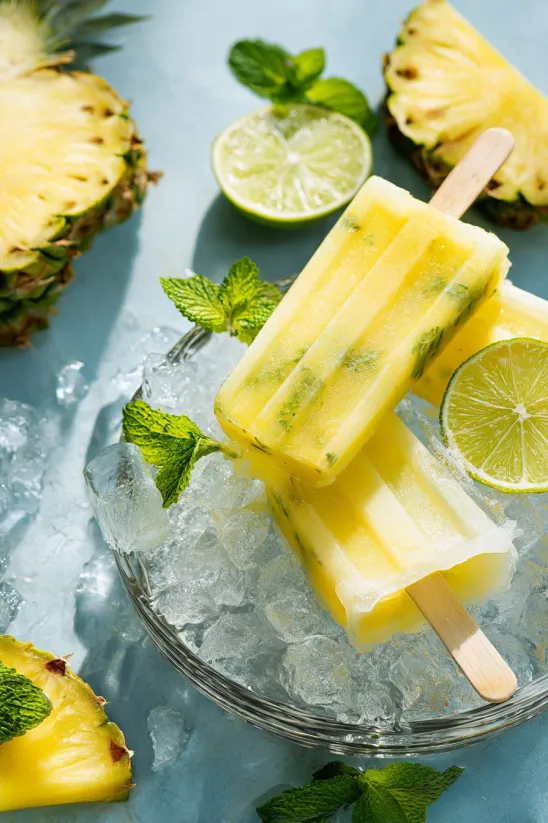 A bowl of pineapple popsicles with limes and mint.