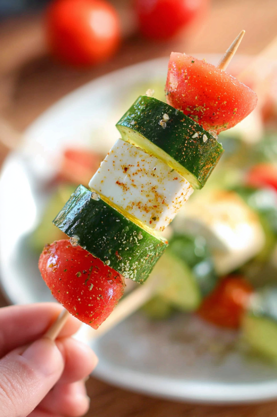 A person holding a stick with a slice of watermelon and a slice of cucumber on it.