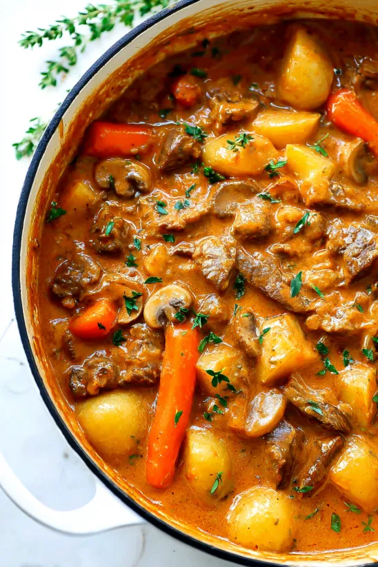 A bowl of stew with meat, potatoes, carrots and mushrooms.