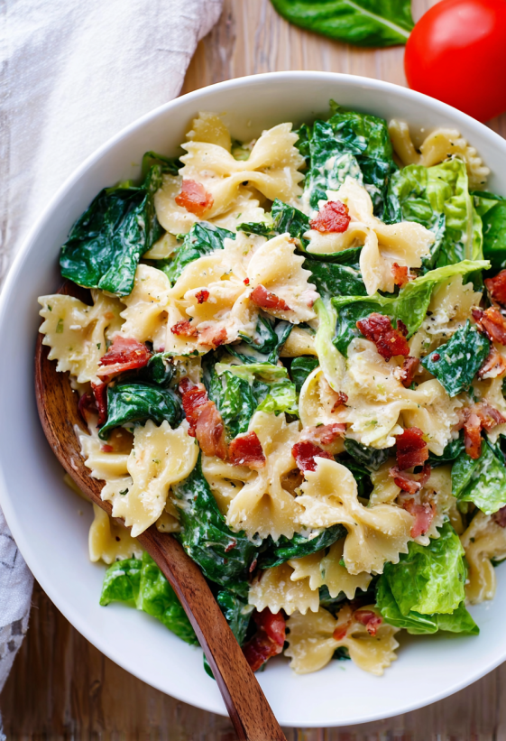 A bowl of pasta salad with bacon and greens.