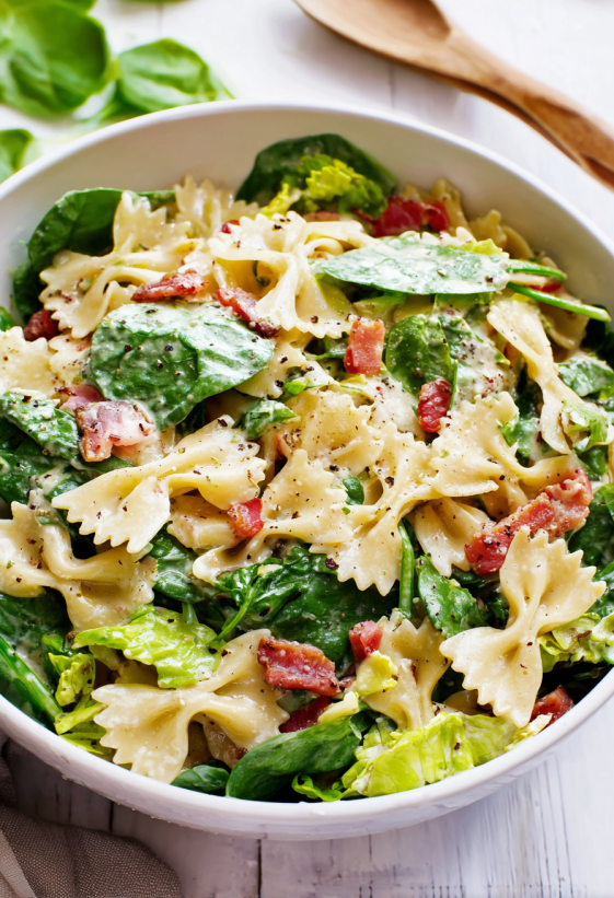 A bowl of pasta salad with bacon and spinach.
