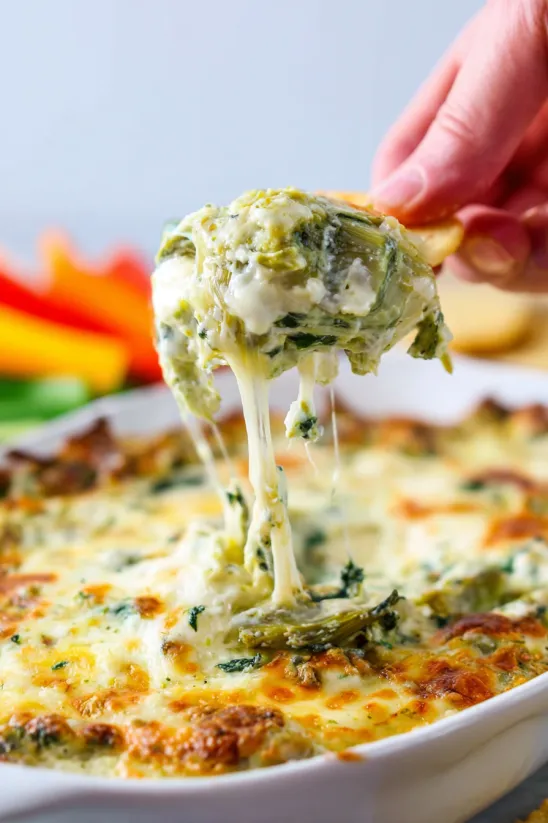 A hand is grabbing a piece of spinach dip.