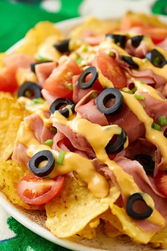 A plate of Irish nachos with ham, olives, tomatoes and cheese.