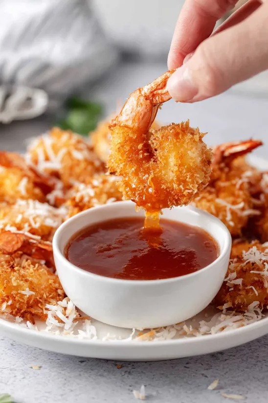 A person is dipping shrimp into a bowl of sauce.