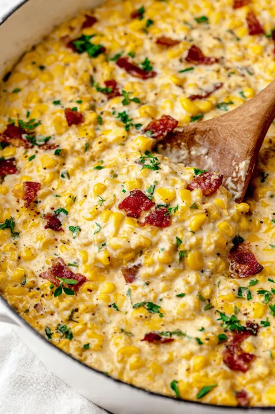A bowl of creamed corn with a wooden spoon in it.