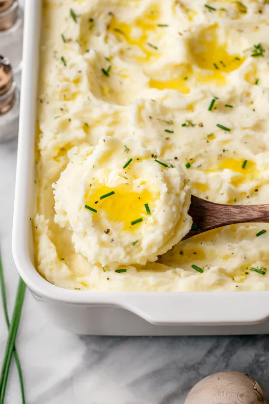 A wooden spoon in a creamy mashed potato dish.