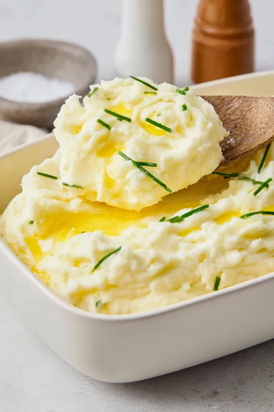 A dish of mashed potatoes with a wooden spoon in it.