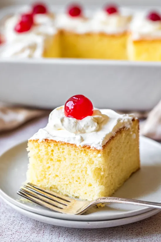 A slice of tres leches cake with a cherry on top.