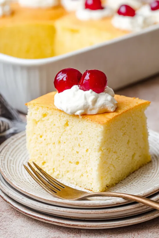 A slice of tres leches cake with whipped cream on top.