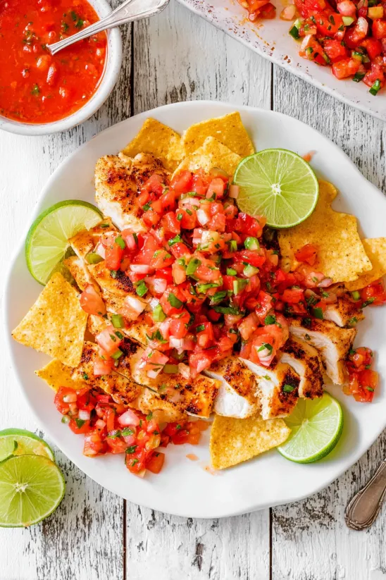 A plate of chicken with tomatoes and limes.