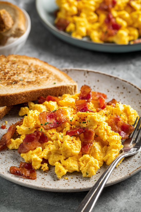A plate of scrambled eggs with bacon and toast.