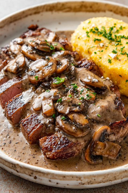 A plate of food with a steak covered in mushroom sauce.