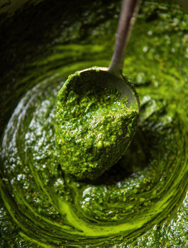 A spoon is in a bowl of green sauce.
