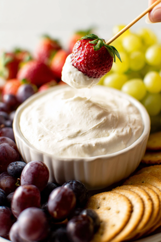 A bowl of cream cheese dip with strawberries on top.
