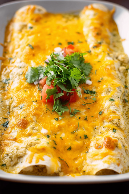 A close up of a sour cream chicken enchilada with tomatoes and green onions.