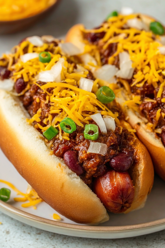 Two chili dogs with cheese and onions.