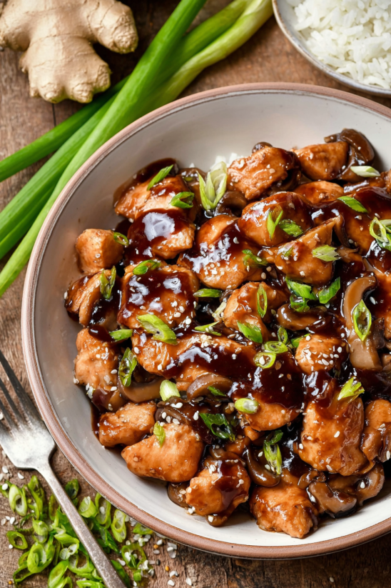 A bowl of bourbon chicken with mushrooms and green onions.