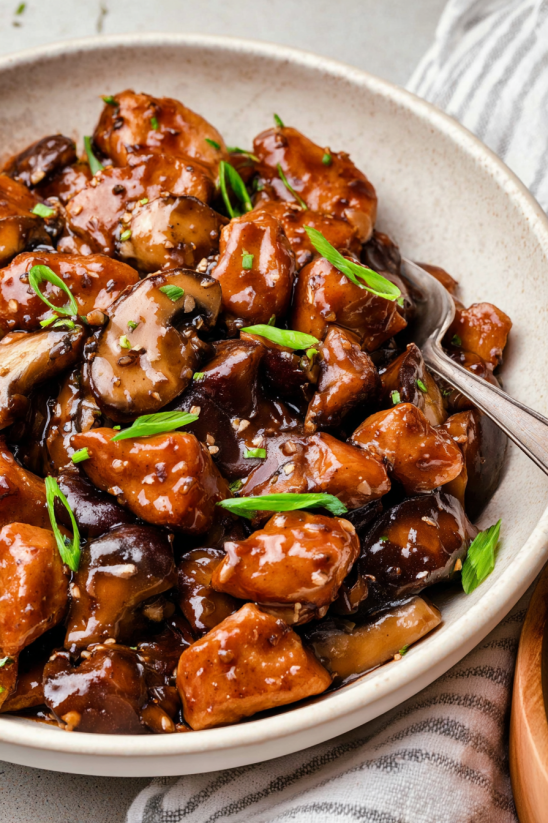 A plate of bourbon chicken with mushrooms and green onions.