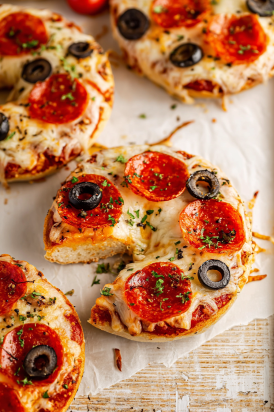 A bagel with pepperoni and olives on top.