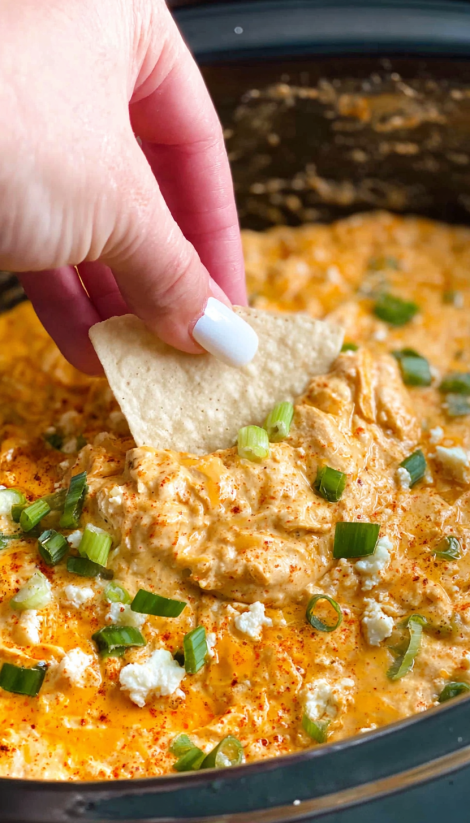 A person is scooping up a tortilla chip from a slow cooker buffalo chicken dip.