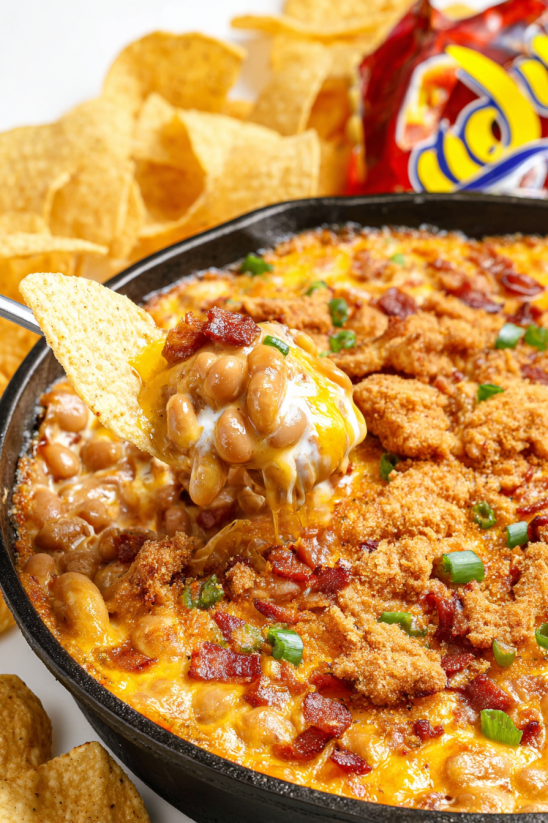 A bowl of chili cheese dip with a spoon in it.