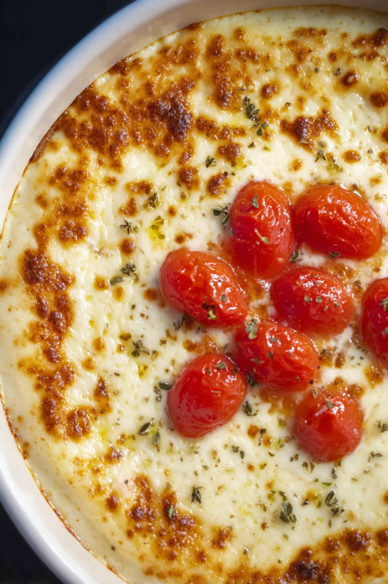 A dish of garlic cheese dip with tomatoes.