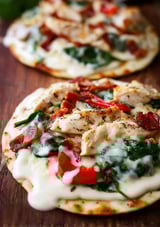 Two pizzas with chicken and vegetables on a wooden table.